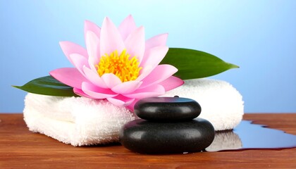 A serene spa scene, featuring a delicate pink lotus flower, smooth dark stones, and a soft white towel, creates a tranquil and inviting atmosphere.