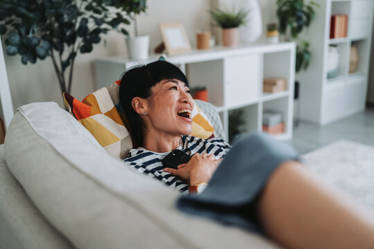 Happy japanese woman relaxing on sofa using smart phone at home