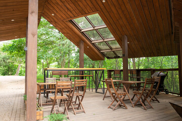 wooden tables and chairs in a cafe under a wooden roof with glass, outdoors in summer