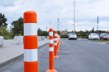 A row of bright orange and white striped traffic cones marking a parking area on a paved road. Roadwork safety barriers.