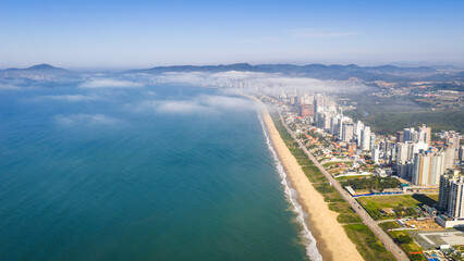Aerial view of Balne&aacute;rio Pi&ccedil;arras shoreline with low fog covering city and beach.
