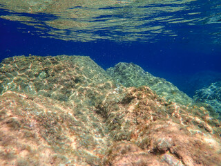 Dark blue ocean surface seen from underwater. Abstract waves underwater and rays of sunlight shining through, Sun light rays undersea deep, Underwater background with sea bottom, Mediterranean sea.