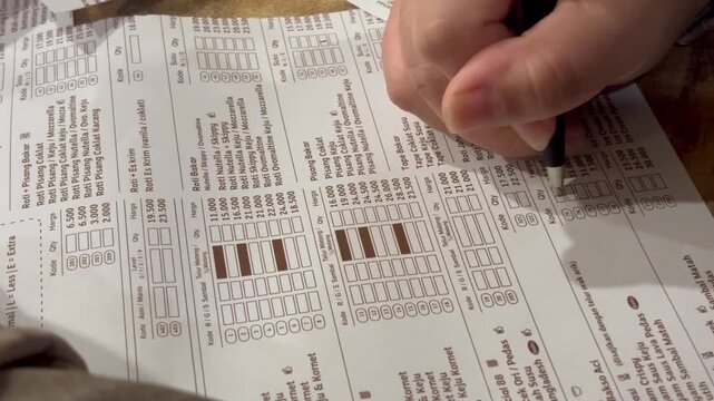 Close-up of a person's hand filling out a food order form with a pen at a restaurant