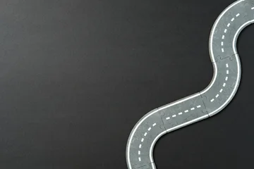 Fotobehang Formule 1 Curved toy road on dark surface with dashed lines. Concept of direction, planning, childhood play, or journey.  © photoguns