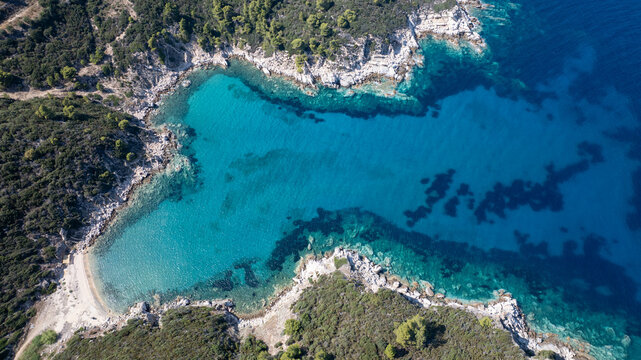 Aerial view of a secluded bay with crystal clear turquoise water, surrounded by a vibrant green coastline in Toroni, Greece