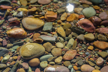 Colorful stones in creek with sun reflecting in water