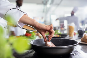 Culinary expert flipping the pork fillet in the pot with tongs and preparing the raw meat on the restaurant kitchen stove. Young professional cooking steak in oil, food industry. Close up.