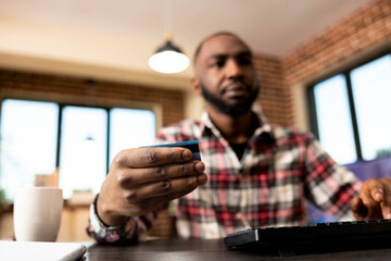 African american businessman typing on keyboard, completing booking reservation by inputting credit card details. Selective focus on black male freelancer making online payments on desktop pc.