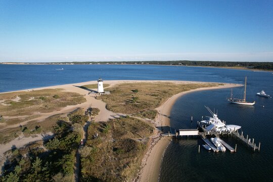 Aerial view of a lighthouse on a sandy peninsula with boats.