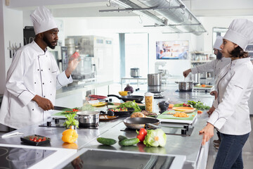 Diverse group of chef chopping vegetables and herbs for meal prep in a commercial restaurant kitchen, using fresh produce and high quality ingredients to create a delicious gourmet dish.