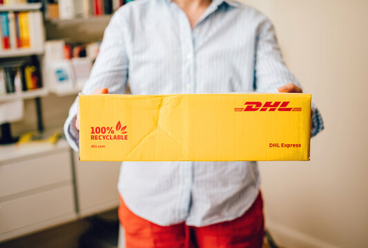 Hamburg, Germany - June 11, 2023: Woman receiving yellow DHL Express parcel with 100 percent recyclable cardboard in her living room - fast worldwide goods e-commerce delivery