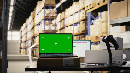 Fulfillment center with chroma key on laptop handling delivery service, order processing with a scanner and computer at the desk. Large business activity with reliable logistics and packaging.