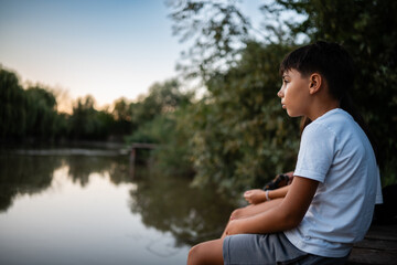 Young boy contemplating nature by the lake at sunset
