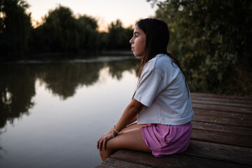 Fototapeta premium Young girl contemplating nature's beauty on a wooden pier at sunset