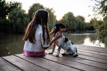 Obraz premium Girl petting her dog while relaxing on a wooden pier by the lake at sunset