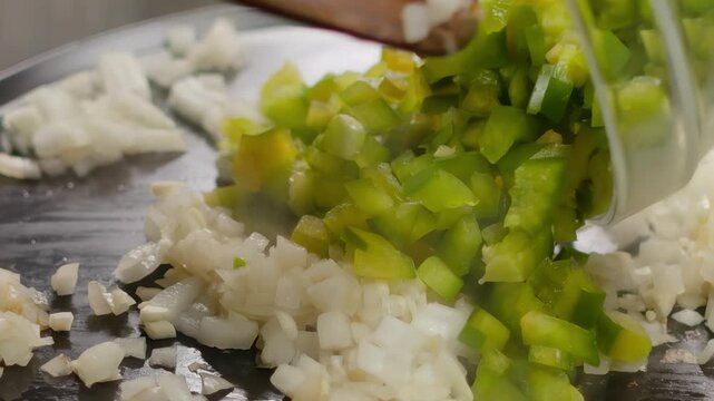 Freshly chopped green bell pepper is added to golden onions frying in a hot pan. Creating a fragrant and flavorful base, a sofrito, for many delicious dishes. Close up