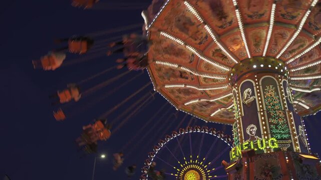  Munich, Germany. Viennese carousel at amusement park during Oktoberfest in evening with beautiful lighting. Wellenflug auf Wiesen Thereianwiese in Munchen. Wellenflieger Oktoberfest. 