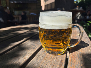 A beer mug illuminated by the sun on a table in a garden restaurant.