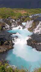 Obraz premium A captivating cascade of turquoise water tumbles over dark volcanic rocks, creating a serene and breathtaking natural spectacle.