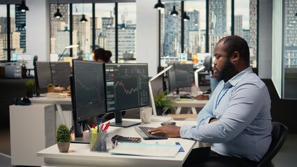 Portfolio manager in prop firm office analyzes stock market trends to enhance investment returns. African american man tracks performance metrics to identify investment opportunities