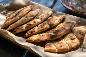 Slices of pita bread seasoned with honey and oregano are arranged on a wooden tray covered with baking paper, ready to be served