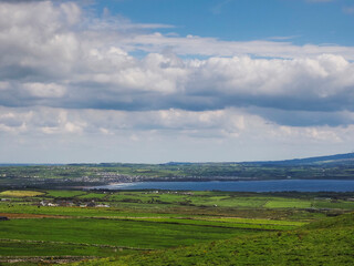 View on lush green fields of Ireland with Lahinch town in the background. Warm sunny day with blue cloudy sky. Irish landscape scene. Nobody. Agriculture private property.