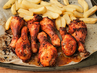 Metal tray with cooked marinated chicken drumsticks and chips. Simple tasty food. Small dinner for a few people. Drumsticks have strong red color and spice herb coating.