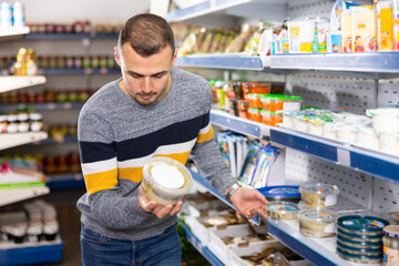 Adult male shopper in casual clothes chooses pickled herring in grocery store