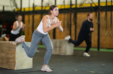 Active young girl practicing one leg squats with box in sports hall during crossfit workout