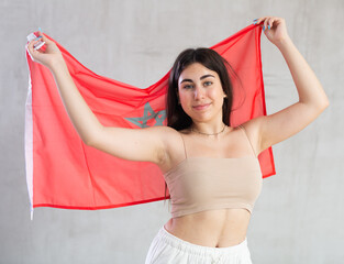 Happy young woman holding large flag of Monaco posing against background of light unicoloured wall