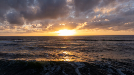 Golden sunset creating a scenic view over the ocean waves near Sintra, Portugal, with dramatic clouds enhancing the beautiful landscape
