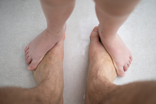 Small child's bare feet standing on top of large adult man's bare feet on white carpet, representing family bond and playful interaction