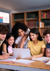 Vertical. Five diverse high school students are smiling and working together on a project in the library, using a laptop and taking notes, demonstrating teamwork and collaboration in education