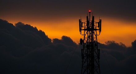 The silhouette of a cell phone tower stands against a dramatic sunset sky. The red warning light at the top of the tower is on.