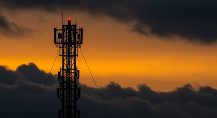 The silhouette of a cell phone tower stands against a dramatic sunset sky. The red warning light at the top of the tower is on.