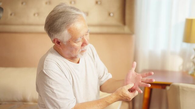 Asian senior man massaging hand, suffering from finger wrist hand pain. Elderly people health problem in joint and tendon pain from rheumatoid arthritis, osteoarthritis and peripheral neuropathy.