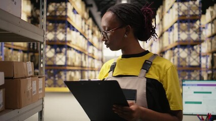 African american female reviewing merchandise data on files for logistics system, distribution hub with organizes shelving, for shipping protocols. Retail fulfillment and supply chain. Camera A. - Powered by Adobe
