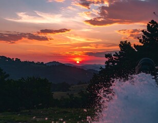 A vibrant sunset paints the hills, showcasing a dramatic sky and a field of water spray.