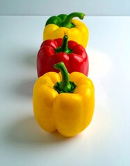 Three vibrant bell peppers in a row against a plain white background, showcasing their bright red, yellow, and green hues.