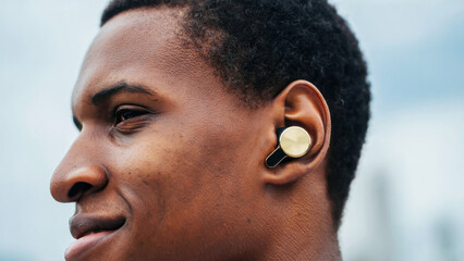 Biowearable device, stealth technology, wireless earbuds, young man outdoors, smart sound gadget, biohacking tool, urban background, modern lifestyle, seamless integration, personal tech