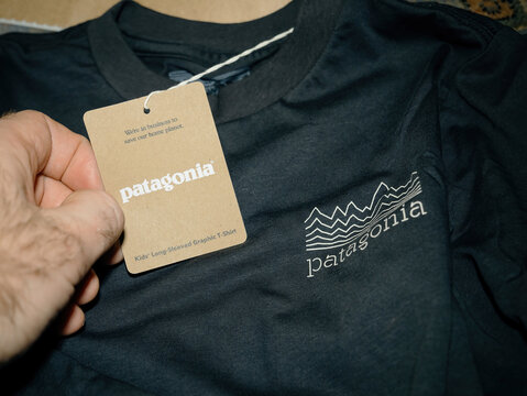 Paris, France - Jan 16, 2025: A hand holding a Patagonia long-sleeve graphic T-shirt with a brown tag featuring the brand's commitment to sustainability and environmental protection.