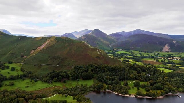 aerial drone shot panning right over catbells mountain in England Lake District surrounded by nature and trees in a valley with mountains in summer with clouded skies