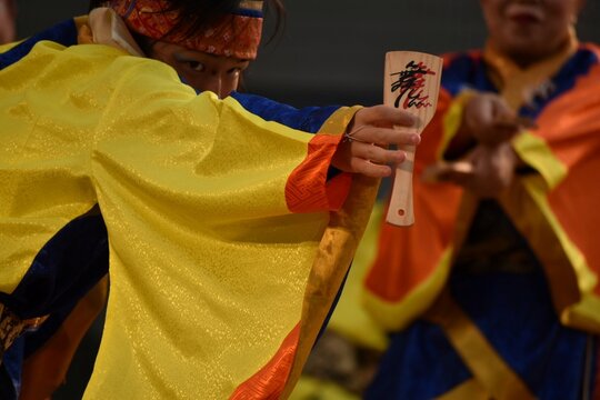 A close-up of a Japanese Yosakoi dancer in a vibrant costume holding naruko clappers during a festival performance. Ideal for concepts of culture, tradition, dance, and celebration.