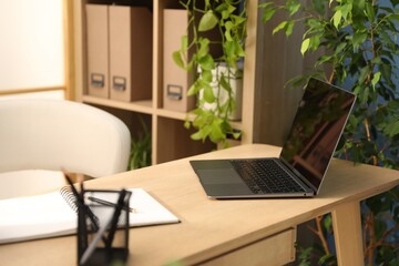 Stylish workplace with laptop, stationery and floral decor in office. Biophilic interior design