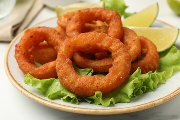 Fried squid rings, lime and lettuce on white marble table, closeup