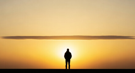 Silhouette of a person standing against a bright orange sunset with a cloud in the distance above