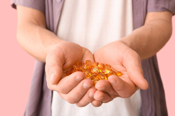 Fototapeta premium Handsome young man with fish oil capsules on pink background, closeup