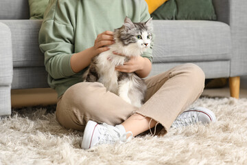 Obraz premium Young woman with cute longhaired cat sitting on floor in living room