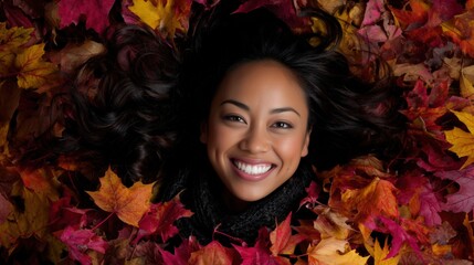 Smiling woman is lying in a bed of autumn leaves with a radiant smile, surrounded by the colorful foliage. This portrait captures the season's essence of joy.