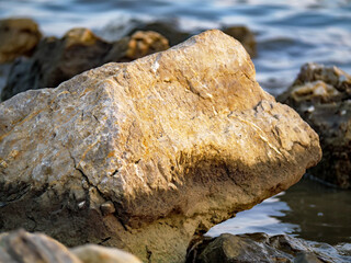 A detailed close-up shot of a large sun-kissed rock on the seashore with the blurred blue sea in the background this photo highlights the stone's warm texture and rugged surface